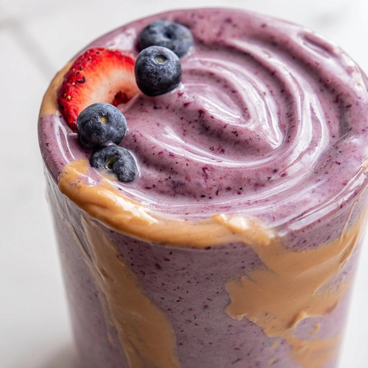 Creamy peanut butter berry smoothie swirled with vibrant red and blue berries in a tall mason jar