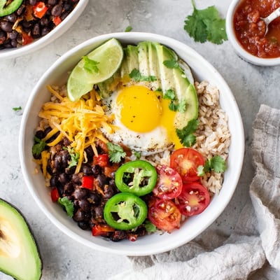 Vibrant Tex Mex Inspired Breakfast Bowls display scrambled eggs, black beans, and fresh avocado slices on a white plate.