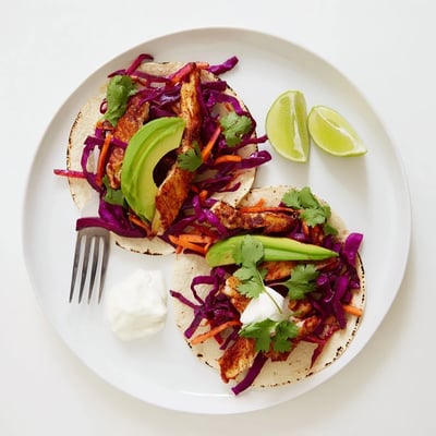 Golden grilled barramundi fillets nestled in soft corn tortillas with lime wedges nearby.