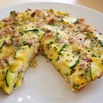 Sliced wedges of Zucchini Herb and Pancetta Frittata are served on a white plate, garnished with fresh herbs and a light salad.