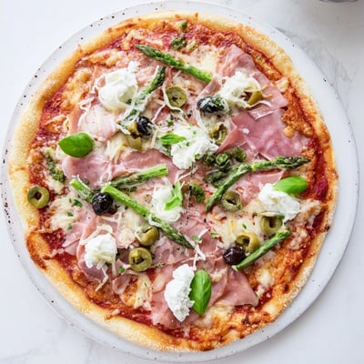 A slice of Ham, Olive, Asparagus, and Ricotta Pizza shows olives, creamy ricotta dollops, and fresh basil garnish.