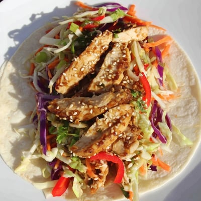 A golden grilled chicken strip peeking from a soft flour wrap filled with crisp red cabbage Thai chicken wraps