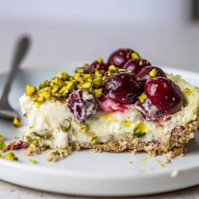 Slice of Lemon Lime Cherry Pistachio Cheesecake shows creamy, zesty filling and speckled crust